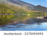 The smooth surface of the lake reflects the forest and blue sky. Wells Gray is a park in the Canadian province of British Columbia in the Rocky Mountains.
