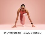 Small photo of Fit young woman standing in start position over pink background. Sportswoman about to start a run.