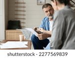 Small photo of Middle aged senior old couple holding documents reading paper bills paying bank loan online, calculating pension fees, payments, taxes, planning family retirement money finances at home.