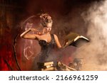 Small photo of Charming woman witch flowers in hair vintage black dress with book of spell in the old castle. Halloween. Celebration. Witchcraft concept, fairy tale mystic atmosphere. Conjure magic spells