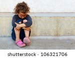 poor, sad little child girl sitting against the concrete wall