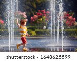 excited redhead baby boy having fun between water jets, in fountain. Summer in the city