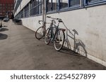 Sunny view of two bicycle lean against wall outside the building on the sidewalk beside the street in Copenhagen. 