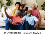 Small photo of Smiling african american three generation family taking a selfie sitting together on couch at home. family, love and togetherness concept, unaltered.