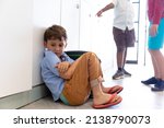 Small photo of Low section of elementary schoolboys bullying caucasian boy wearing slipper while sitting on floor. unaltered, childhood, bullying, problems, sadness, cruel, education and back to school concept.