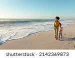 Full length of african american mother and daughter walking on shore at beach with copy space. unaltered, family, lifestyle, togetherness, enjoyment and holiday concept.
