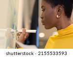 Confident african american businesswoman writing strategy on whiteboard at workplace. unaltered, business and modern office concept.