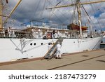 Small photo of Gdynia, Poland - May 27, 2022: Tall-ship Dar Mlodziezy moored at the wharf in the port. The crew operates the gangplank at the side. This is a three-masted Polish training sailing ship, frigate type.