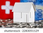Model of a detached house made of paper on a background of Swiss franc banknotes, coins and the symbolic Swiss flag can mean real estate, mortgage or just a paper toy or other real estate meaning