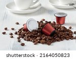 Closeup of roasted coffee beans and coffee capsules for a capsule coffee machine. On a light background with espresso cups.