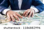 Small photo of Conceptual image of greed and avarice. Businessman grabbing money lying on office desk