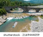 Small photo of Aerial view. Drought and dry rivers. Roman bridge of Bobbio over the Trebbia river, Piacenza, Emilia-Romagna. Italy. 06-16-2022. River bed with stones and vegetation. Called hunchback bridge
