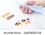 Small photo of Various pills and the hand of a old ill woman with the ineffectual mask on a medical bedsheet
