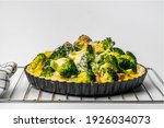 View of freshly baked homemade broccoli salmon quiche in metal oven pie baking plate on white background.