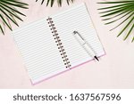 Small photo of Flat lay open empty note book and white pen on light pink background with green tropival foliage, top view, copy space