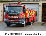 Small photo of RONNEBY, SWEDEN - OCTOBER 26, 2014: Firefighter in shorts and tshirt walking to fire truck outside station building. Truck is red and yellow Scania 114G.