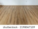 Small photo of Laminated wood floor with white wall. Empty room with floating laminate in new apartmen