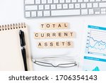 Small photo of Total current assets concept with letters on cubes. Still life of office workplace with supplies. Flat lay grey surface with computer keyboard and notepad. Capital investment and financial analytics.