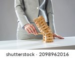 Businesswoman removing wooden block from falling tower on table. Management of risks and economic instability concept with wooden jenga game. Failure and collapse in corporate business