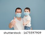young father and his toddler son wearing surgical masks giving thumbs up to protection during the quarantine on a blue background
