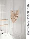 Small photo of Clothing rail with pointes, ballet body suit and dress. Ballet class or ballet store concept. Light interior with barre and ballet accessory