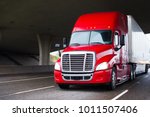 A modern big rig semi truck for long haulage with a high cabin for improving aerodynamic characteristics moves under the bridge transporting a dry van semi trailer with commercial cargo