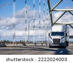 Big rig industrial powerful semi truck transporting commercial cargo in dry van semi trailer climbing on the arched overpass highway road intersection bridge with cable support