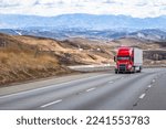 Small photo of Industrial long hauler big rig green semi truck tractor with chrome parts transporting commercial cargo in loaded dry van semi trailer climbing uphill on the mountain highway road in California