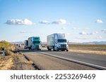 Industrial commercial big rigs long hauler semi trucks with semi trailers transporting different cargo driving on the wide divided straight highway road between the fields in California