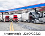 Small photo of Industrial standard big rigs semi trucks with semi trailers standing on the fuel station parking lot filling the semi trucks tanks with diesel fuel to have ability continue commercial flight