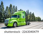 Small photo of Industrial grade professional use bright green powerful big rig semi truck tractor without the semi trailer running on the wide highway road to warehouse for picking up the next freight load