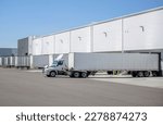 Small photo of Industrial big rig day cab semi truck tractor with roof spoiler and semi trailers standing on the warehouse parking lot loading cargo for start off the next freight according to the schedule