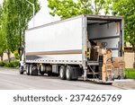 Small photo of White classic industrial local carrier day cab big rig semi truck tractor delivering commercial cargo in dry van semi trailer standing on the city street road