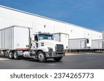 Small photo of Industrial standard powerful day cab local carrier big rig white semi truck tractor hooks a loaded dry van semi trailer in warehouse dock gates area at sunny day