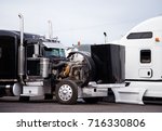 Small photo of Large black classic big rig semi truck with an open hood is on a technical inspection of the engine to prepare truck and make sure that everything works properly for the next commercial cargo delivery