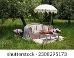 A romantic date for lovers, a picnic in the spring garden, a wedding. A sofa with pillows and a table in nature among apple trees, flowers and grass.