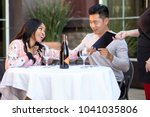 Small photo of Interracial couple on a date paying for a restaurant tab with a waitress. They are in an outdoor cafe handling the payment bill and server tip or gratuity.
