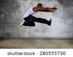 Black urban hip hop dancer jumping high on a concrete background.  The man is doing parkour or leaping.