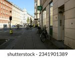 Small photo of COPENHAGEN, DENMARK - JULY 9, 2023: Two cyclists pass along the street. Bicycles are parked outside the 365 Coop discount store (is the cheapest discount chain).