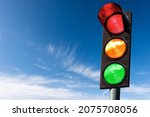 Closeup of a traffic light on a blue sky with clouds and copy space, with all three lights on, green, orange and red. Italy, Europe.