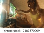 Small photo of Happy woman pouring water onto hot stone in a wooden barrel sauna. Steam on the stones, spa and wellness concept, girlfriends relaxing in hot finnish ssauna cabin. Warm temperature bath therapy.