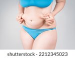 Small photo of Tummy tuck, flabby skin on a fat belly, plastic surgery concept on gray background