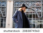 Lifestyle portrait of fashionable woman wearing winter or spring outfit, felt hat, gray wool coat, turtleneck. Outdoors. Female stylish Model smiling, walking city Street. Fashion trend