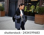 Small photo of Stylish fashion woman strolls down the street in multilayer clothes oversized blazer, black leggings. Fashionable outfit, street style.