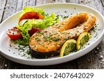 Fried salmon steak and fresh vegetable salad served on wooden table 