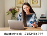 Shot of happy woman holding a bank card in her hand and using laptop while shopping online. 