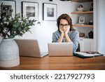 Small photo of Worried woman sitting at laptops and hands on face. Careworn business woman working from home. Home office.