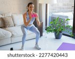 Beautiful slim fitness woman crouches with dumbbells. Sport, healthy lifestyle. Girl goes in for sports at home