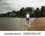 Cheerful young woman with long hair walks by the lake barefoot. Splashing on the shore. Fun and summer time