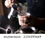 Barista pouring coffee from moka pot coffee maker to a coffee cup. Hand holding Italian classic moka pot pouring coffee.